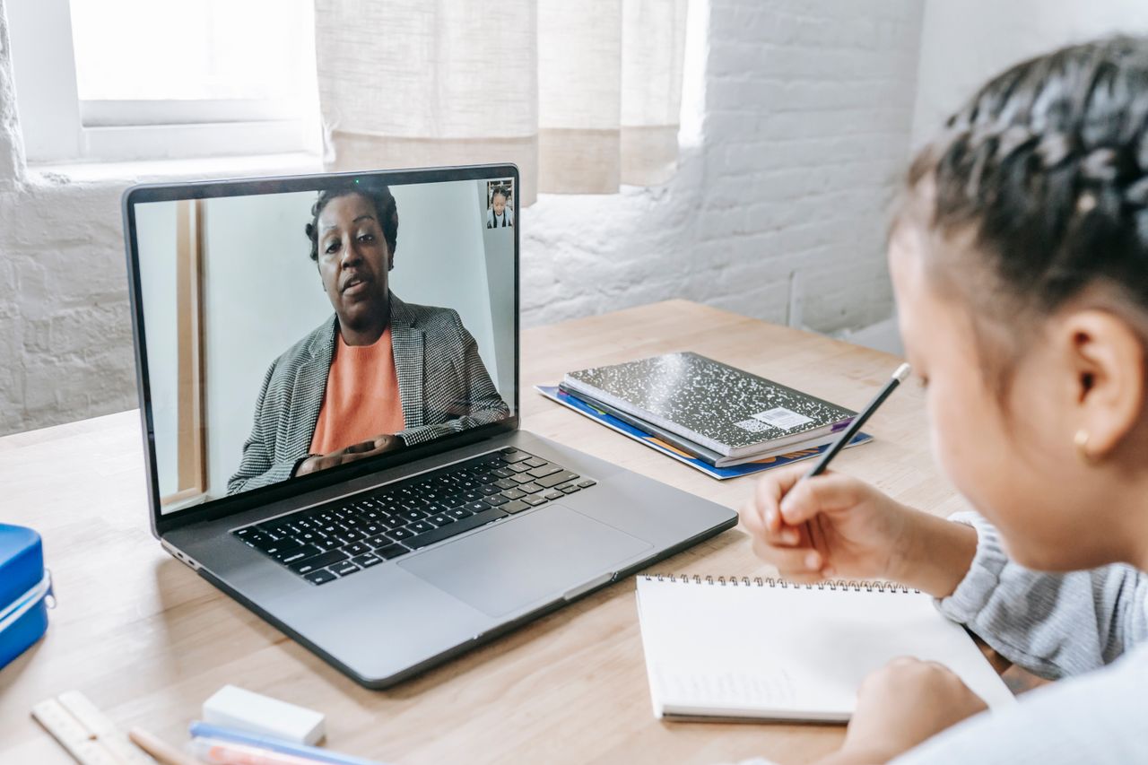 Vue arrière d'une jeune fille ethnique concentrée, prenant un examen avec un tuteur via internet sur un netbook.